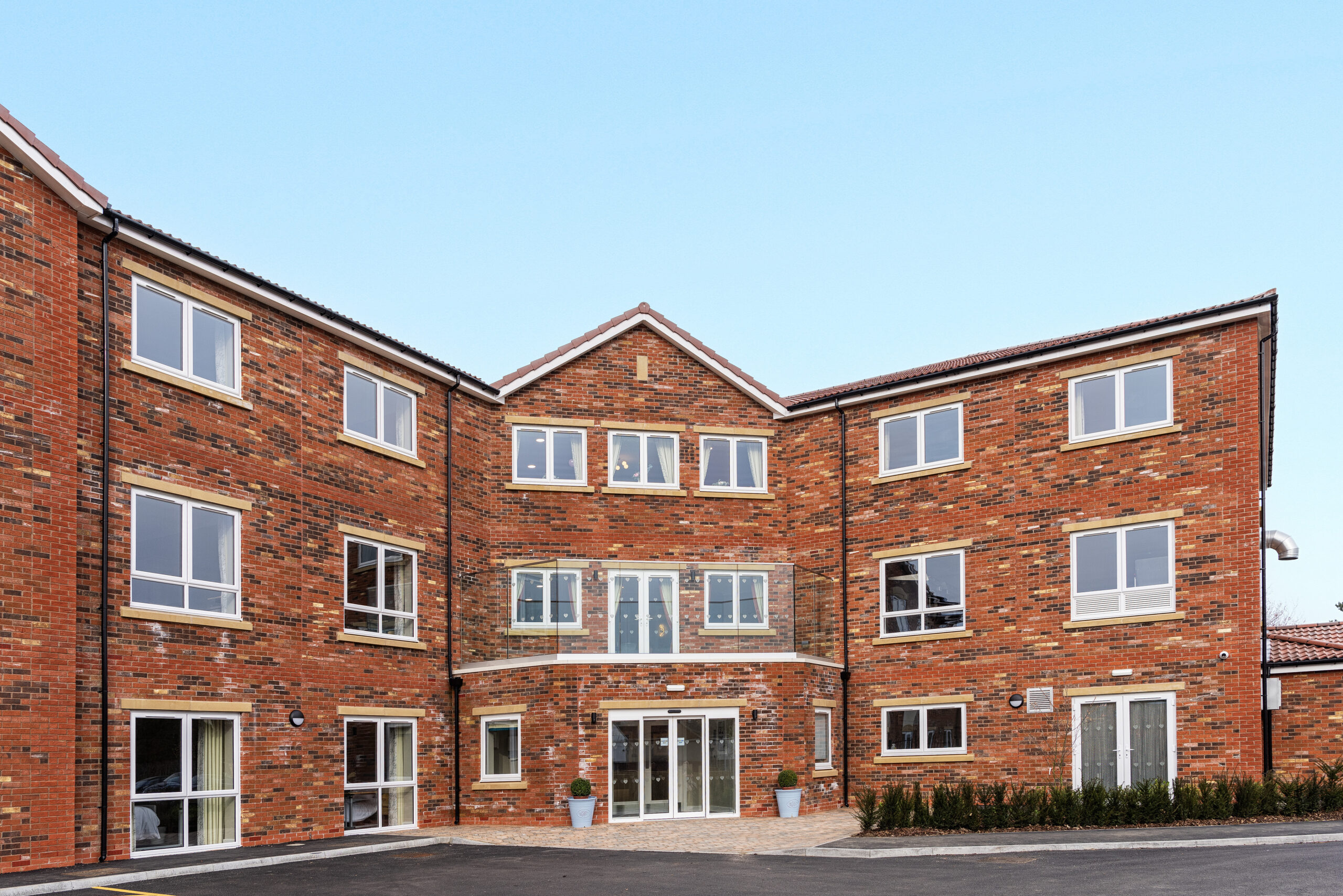 Exterior view of Sleaford Hall Care Home, a modern three-story building located in Sleaford, Lincolnshire. The facility is surrounded by well-maintained gardens and features large windows that provide natural light. The entrance is welcoming, reflecting the care home's commitment to comfort and hospitality.